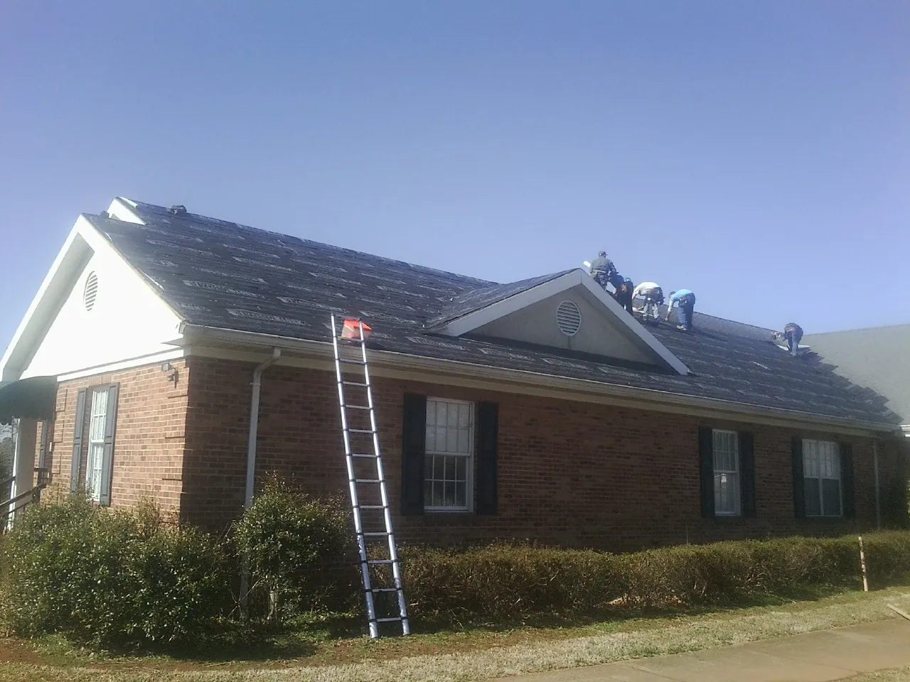 Crew tearing shingles off a brick ranch roof with a ladder set — Metal Roof Repair work by our crew in Green Bay