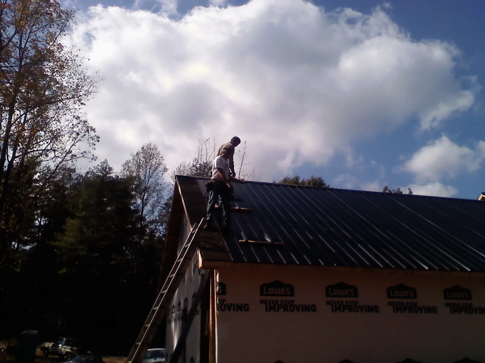 Roofer fastening dark metal panels high against a cloudy sky, from a Roof Inspection job in Green Bay