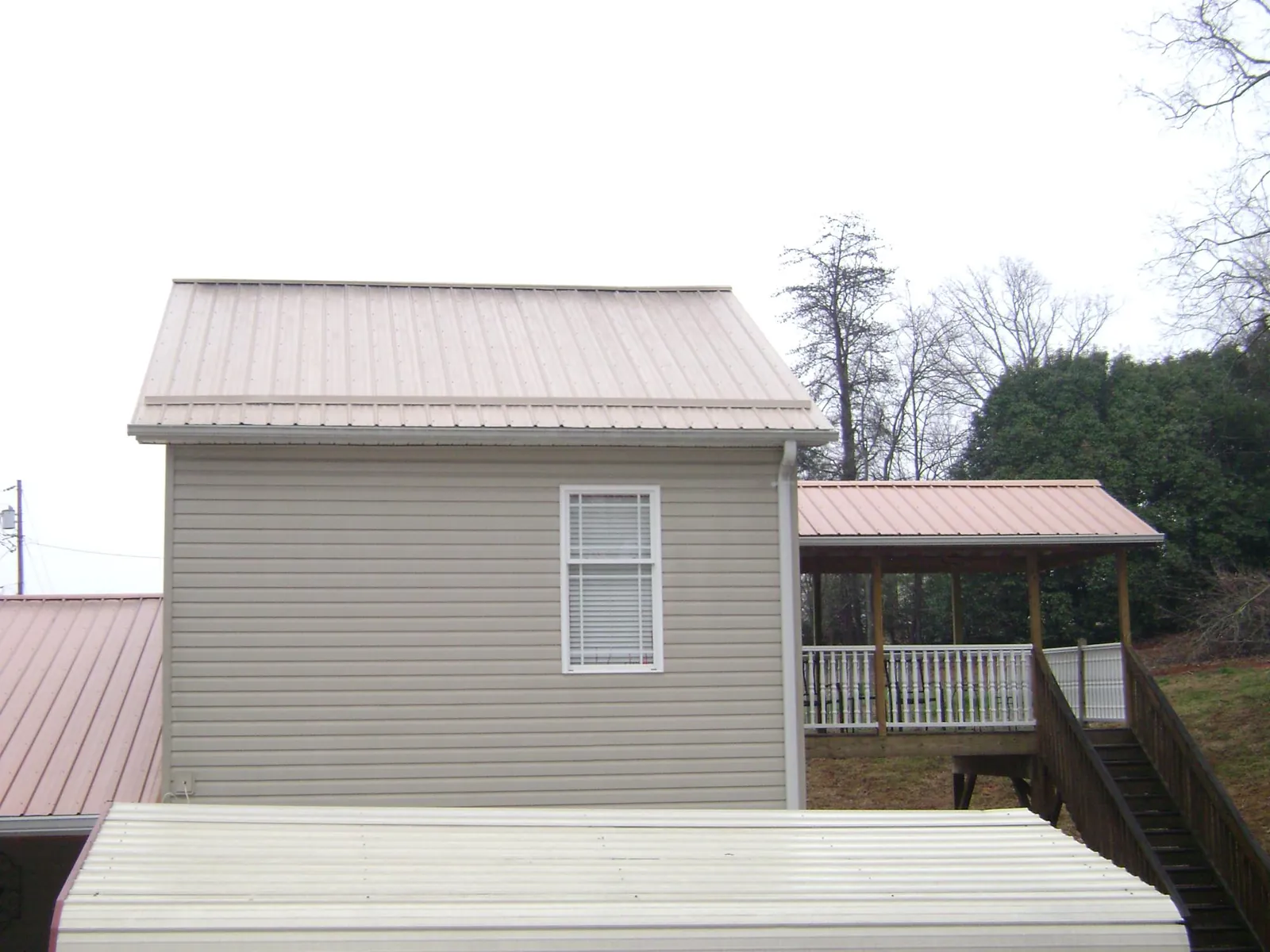Tan metal roofs on a two story addition and attached porch, from a Roof Replacement job in Green Bay